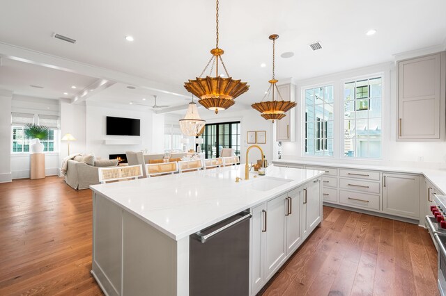 kitchen featuring hardwood / wood-style floors, a kitchen island with sink, a lit fireplace, a sink, and appliances with stainless steel finishes