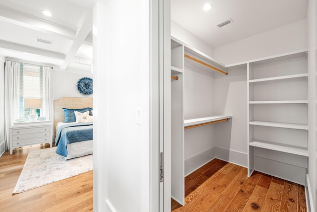 spacious closet with visible vents, coffered ceiling, and wood finished floors