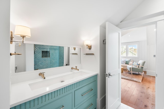 bathroom with wood finished floors, lofted ceiling, double vanity, a shower with shower door, and a sink