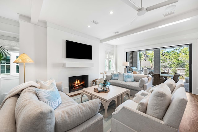 living room with visible vents, a fireplace with flush hearth, beamed ceiling, and wood finished floors