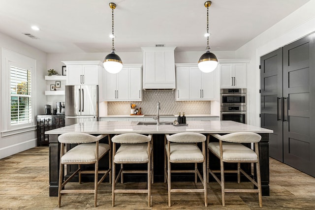 kitchen featuring appliances with stainless steel finishes, a center island with sink, white cabinetry, and hanging light fixtures