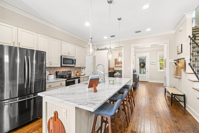 kitchen with appliances with stainless steel finishes, white cabinetry, decorative light fixtures, and an island with sink