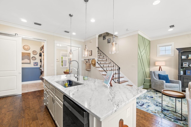 kitchen with decorative light fixtures, dark wood-type flooring, sink, and an island with sink