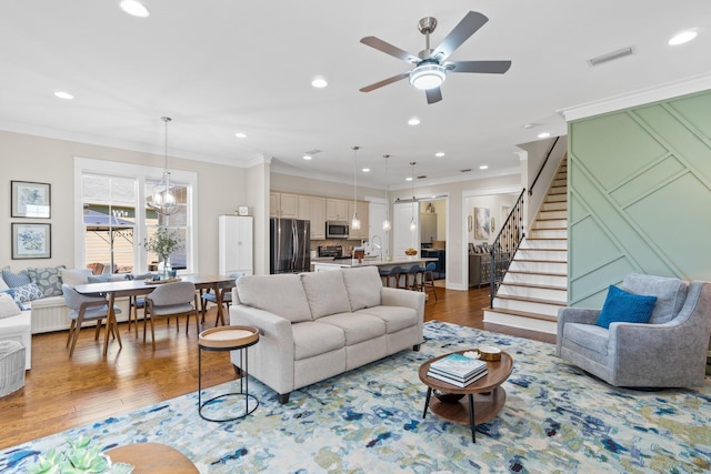 living room featuring crown molding, sink, wood-type flooring, and ceiling fan with notable chandelier