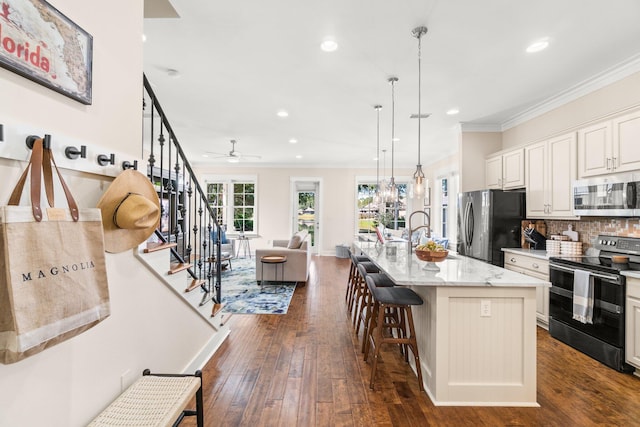 kitchen with stainless steel appliances, pendant lighting, dark wood-type flooring, light stone counters, and a center island with sink