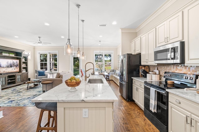 kitchen with appliances with stainless steel finishes, ornamental molding, dark wood-type flooring, and a large island with sink