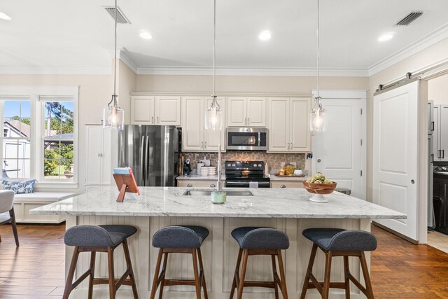 kitchen featuring a large island with sink, appliances with stainless steel finishes, a barn door, dark hardwood / wood-style flooring, and hanging light fixtures