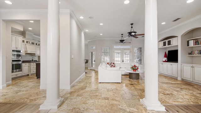 living room featuring light wood-type flooring, decorative columns, ornamental molding, ceiling fan, and built in features