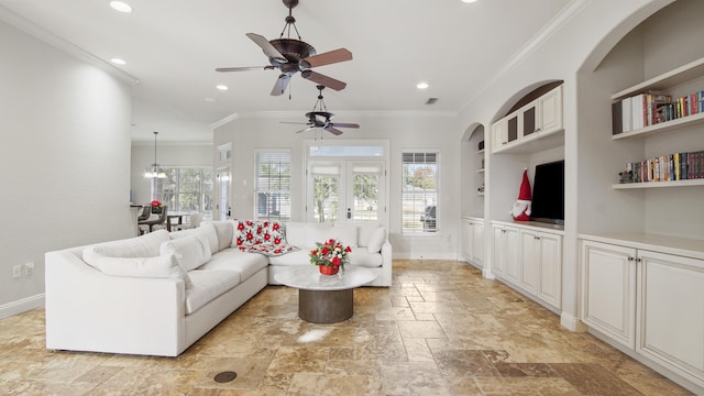 living room featuring built in shelves, ceiling fan with notable chandelier, plenty of natural light, and crown molding