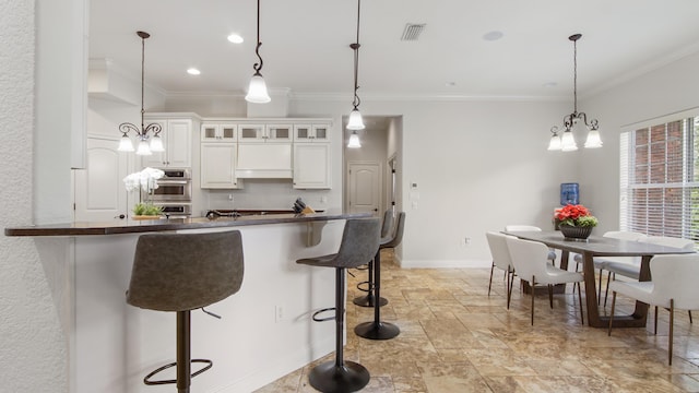 kitchen featuring a kitchen breakfast bar, ornamental molding, decorative light fixtures, a chandelier, and white cabinetry