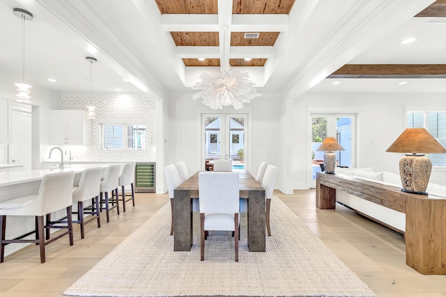 dining space featuring coffered ceiling, beam ceiling, light hardwood / wood-style flooring, wine cooler, and an inviting chandelier