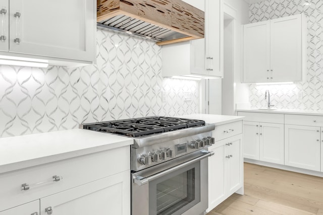 kitchen featuring decorative backsplash, high end range, light wood-type flooring, white cabinetry, and premium range hood