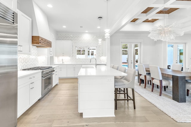 kitchen with a kitchen island with sink, decorative light fixtures, light wood-type flooring, and premium appliances