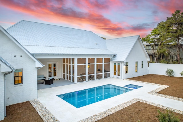 back house at dusk featuring french doors, a patio, and a sunroom