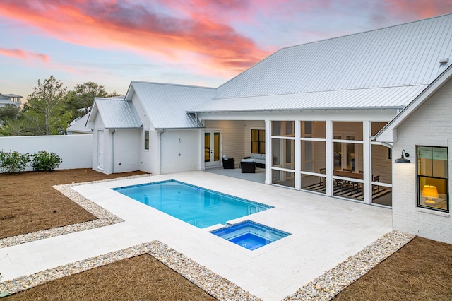 pool at dusk with a patio, an in ground hot tub, and a sunroom