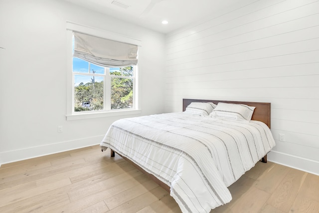 bedroom with light wood-type flooring and wood walls