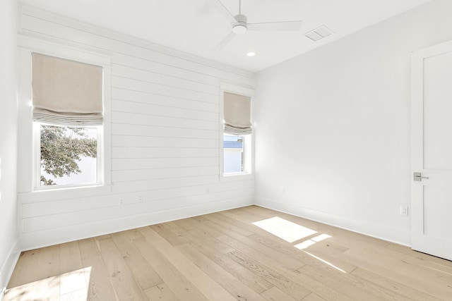 spare room with wooden walls, light hardwood / wood-style flooring, a healthy amount of sunlight, and ceiling fan