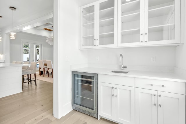 bar with hanging light fixtures, light wood finished floors, wine cooler, and a sink