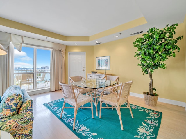 dining space featuring a tray ceiling, a city view, visible vents, light wood-style floors, and baseboards