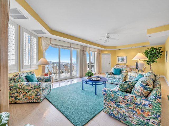 living room featuring a tray ceiling, visible vents, ceiling fan, and wood finished floors