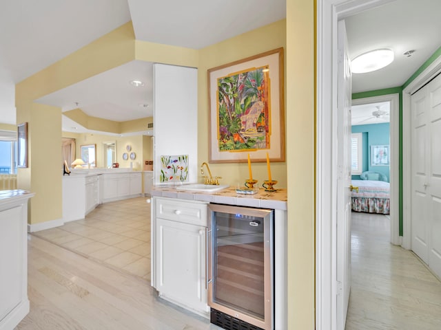 bar featuring beverage cooler, baseboards, light wood-style floors, bar area, and a sink