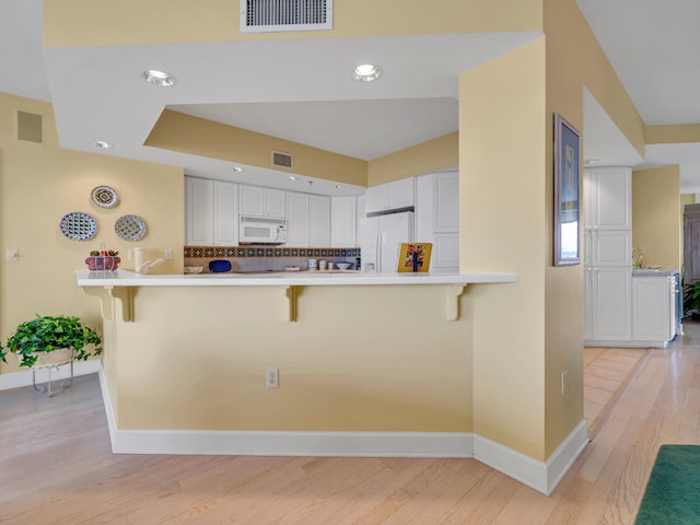 kitchen featuring a peninsula, white appliances, visible vents, and a kitchen breakfast bar