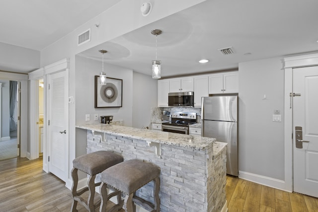 kitchen with hanging light fixtures, appliances with stainless steel finishes, light hardwood / wood-style floors, and white cabinets