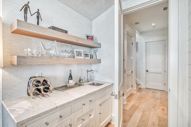 bar with tasteful backsplash, sink, white cabinets, light stone countertops, and light wood-type flooring