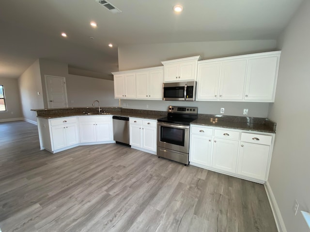 kitchen with kitchen peninsula, appliances with stainless steel finishes, white cabinetry, vaulted ceiling, and light hardwood / wood-style flooring