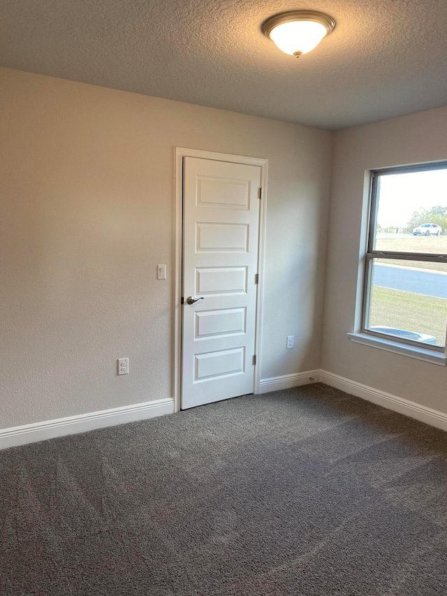 spare room with a textured ceiling and dark carpet