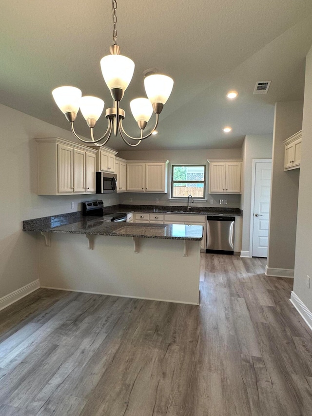 kitchen with kitchen peninsula, appliances with stainless steel finishes, hardwood / wood-style flooring, pendant lighting, and sink