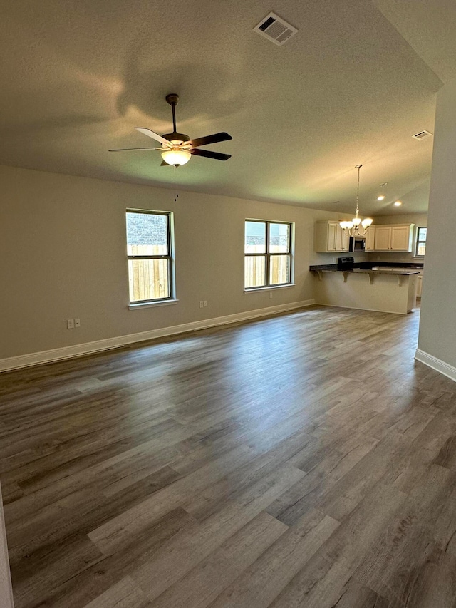 unfurnished living room featuring a healthy amount of sunlight, dark hardwood / wood-style flooring, and ceiling fan with notable chandelier