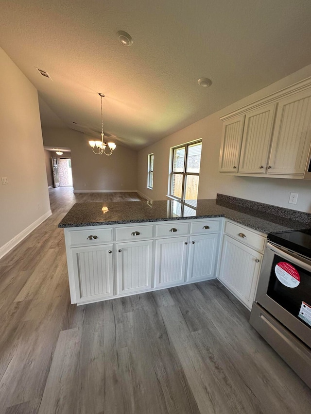 kitchen featuring lofted ceiling, hardwood / wood-style floors, kitchen peninsula, an inviting chandelier, and stainless steel stove