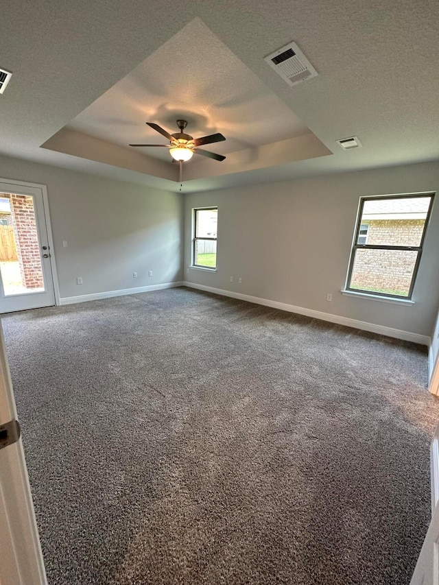 carpeted spare room with a textured ceiling, a tray ceiling, and ceiling fan