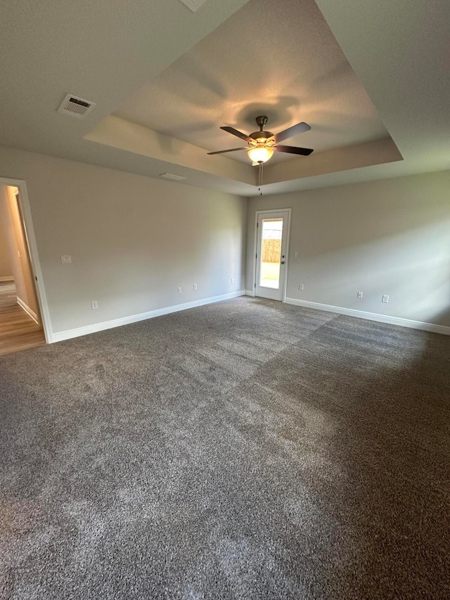 unfurnished room featuring a textured ceiling, ceiling fan, dark carpet, and a raised ceiling