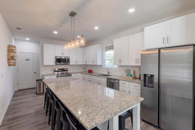 kitchen featuring appliances with stainless steel finishes, a kitchen island, pendant lighting, white cabinets, and a breakfast bar