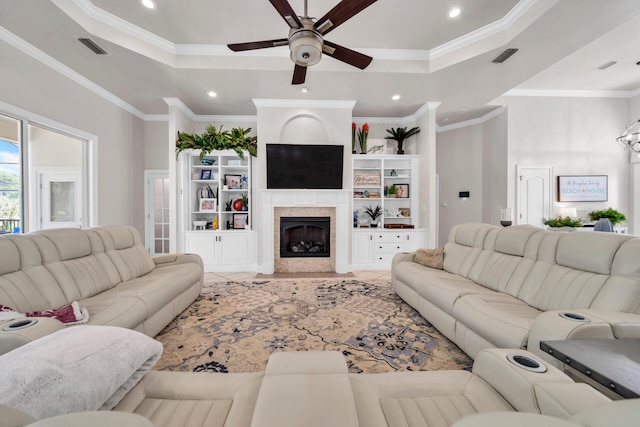 living room featuring a tiled fireplace, a raised ceiling, ornamental molding, and ceiling fan