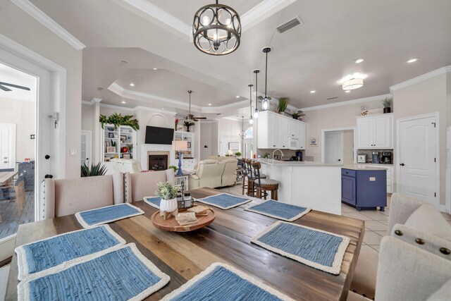 dining room featuring a raised ceiling, light wood-type flooring, ornamental molding, a fireplace, and ceiling fan with notable chandelier