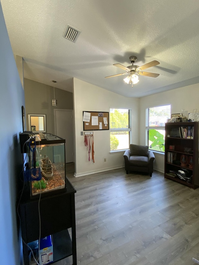 living area with lofted ceiling, ceiling fan, wood-type flooring, and a textured ceiling