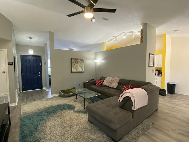 living room with wood-type flooring, vaulted ceiling, a textured ceiling, and ceiling fan