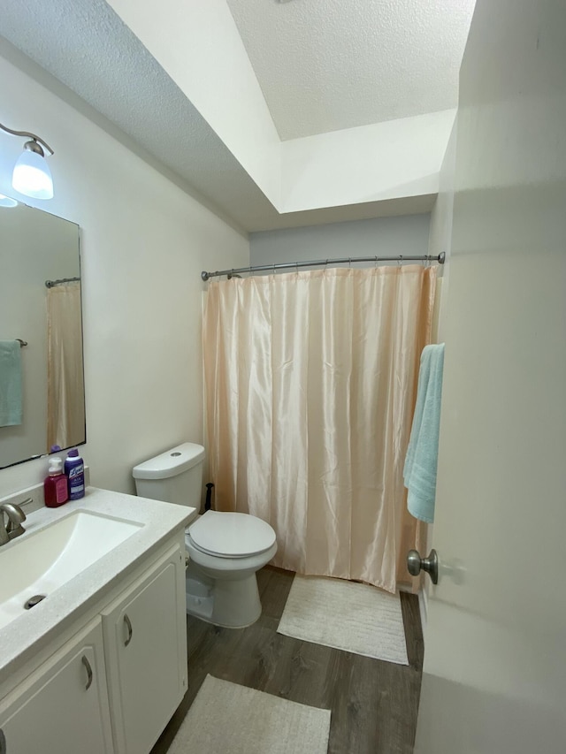 bathroom featuring curtained shower, wood-type flooring, vanity, toilet, and a textured ceiling