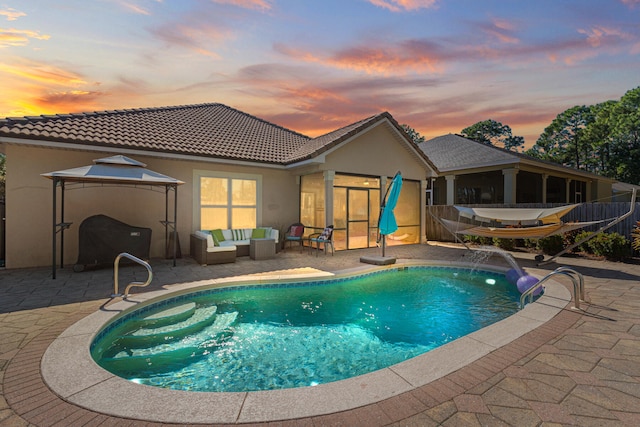 pool at dusk featuring an outdoor living space, pool water feature, and a patio area