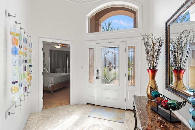 foyer with a towering ceiling, ceiling fan, and light tile patterned floors