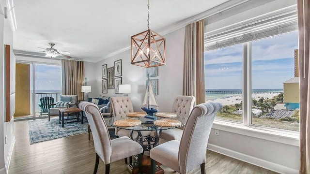 dining space with a water view, hardwood / wood-style flooring, ornamental molding, and ceiling fan with notable chandelier