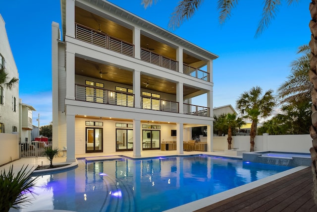 back house at dusk featuring a patio area, a balcony, and a swimming pool with hot tub