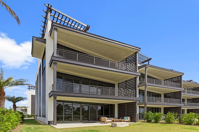 rear view of property featuring a balcony, an outdoor living space with a fire pit, a patio, and a lawn