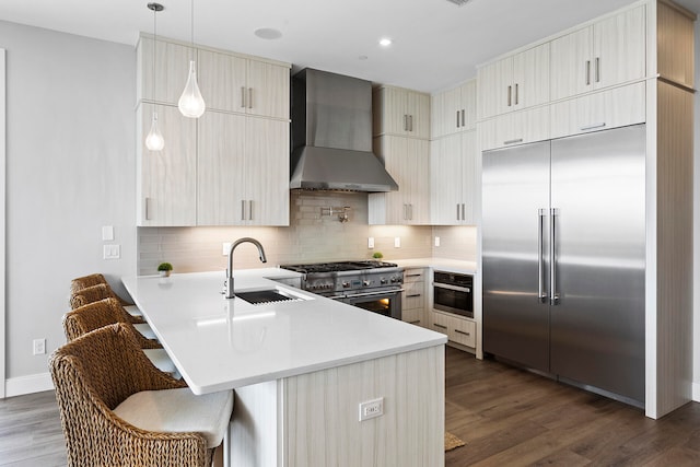 kitchen with wall chimney exhaust hood, dark hardwood / wood-style floors, high quality appliances, and kitchen peninsula