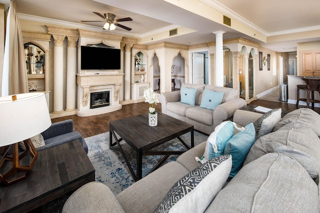 living room featuring dark wood-type flooring, ornate columns, a raised ceiling, and crown molding