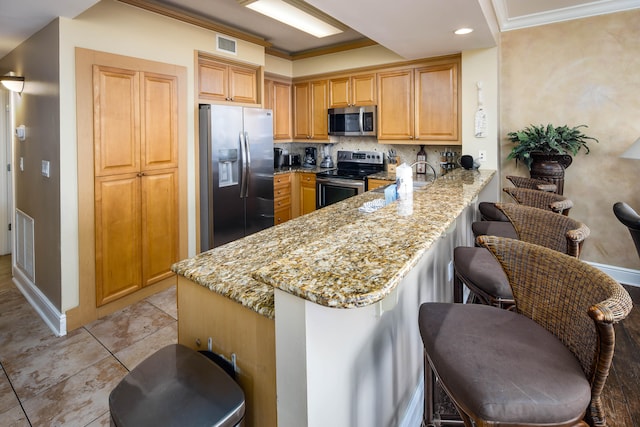 kitchen with a kitchen bar, kitchen peninsula, stainless steel appliances, light stone counters, and ornamental molding