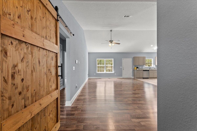 unfurnished living room with ceiling fan, a textured ceiling, dark hardwood / wood-style flooring, and a barn door